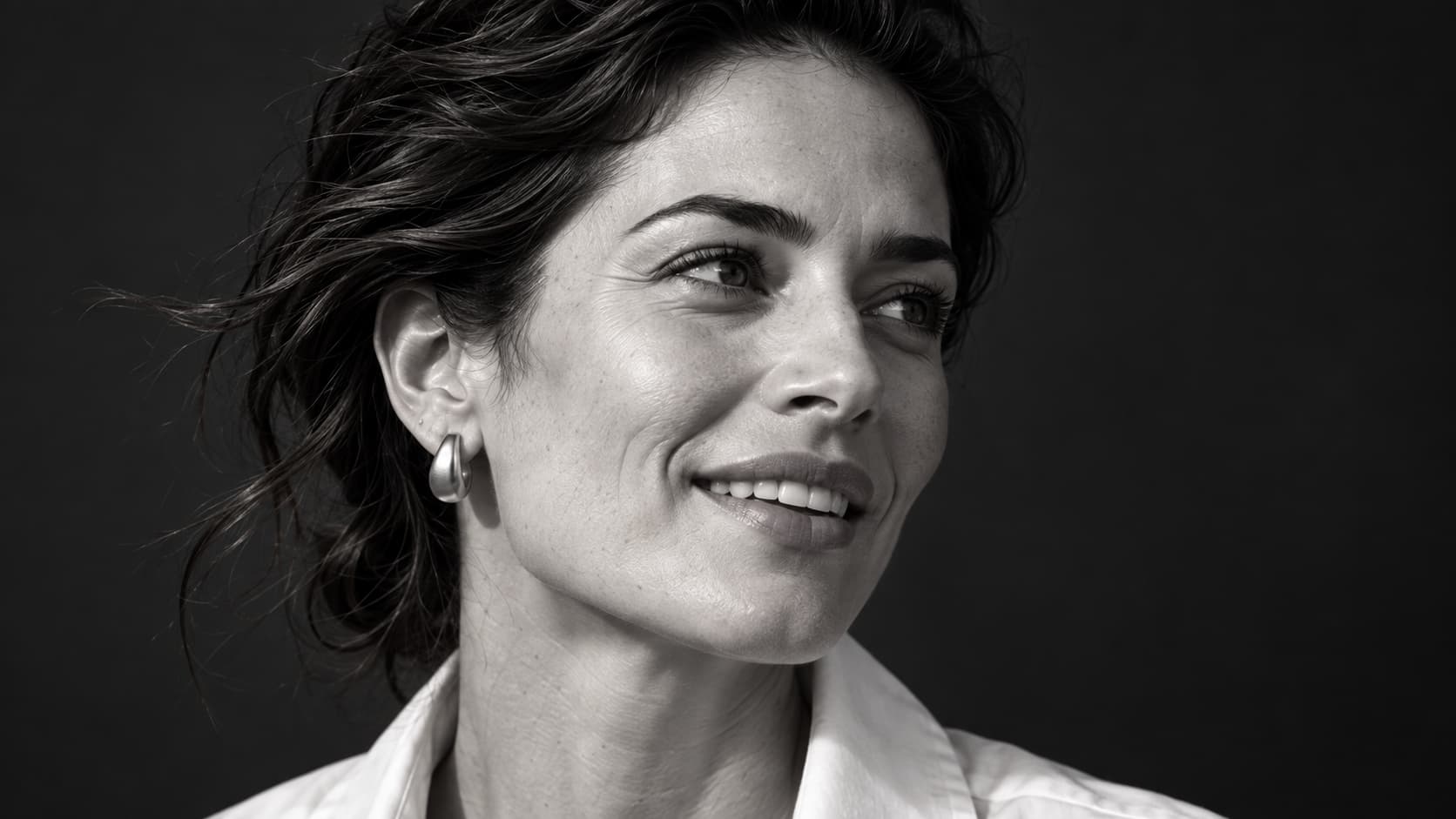 Primer plano en blanco y negro de una mujer que sonríe, con la mirada hacia un lado.